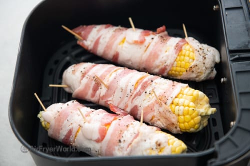 Uncooked bacon wrapped corn in air fryer basket