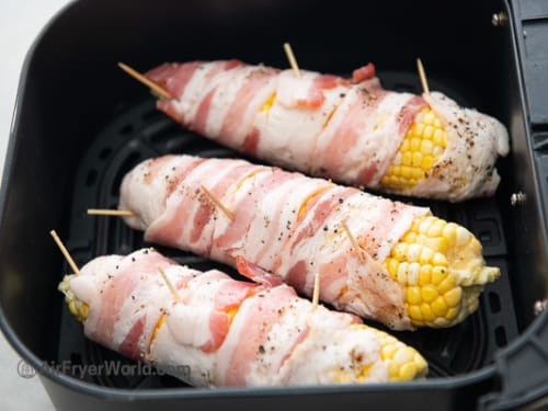 Uncooked bacon wrapped corn in air fryer basket