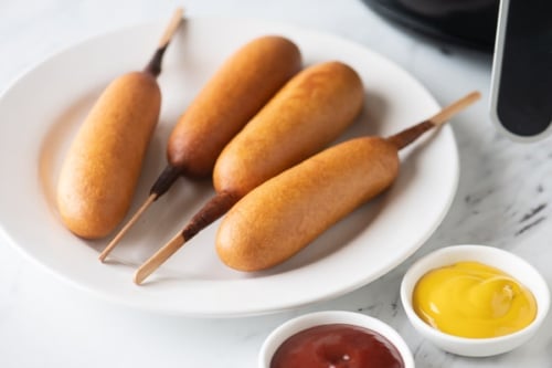 Cooked full sized corn dogs on plate with ketchup and mustard
