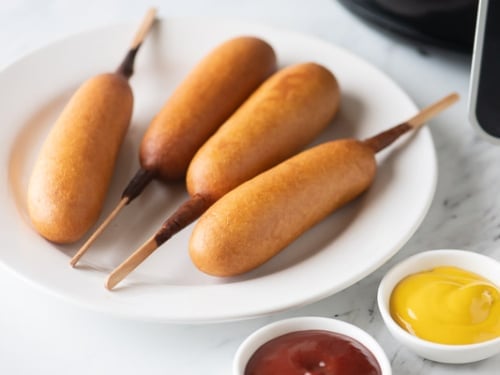 Cooked full sized corn dogs on plate with ketchup and mustard