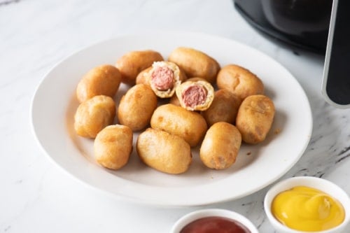 Cooked mini corn dogs on plate with ketchup and mustard