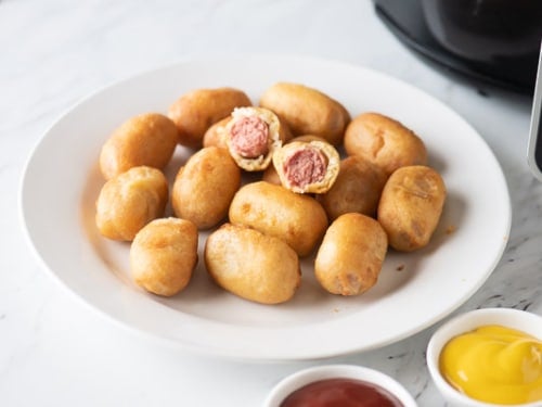 Cooked mini corn dogs on plate with ketchup and mustard