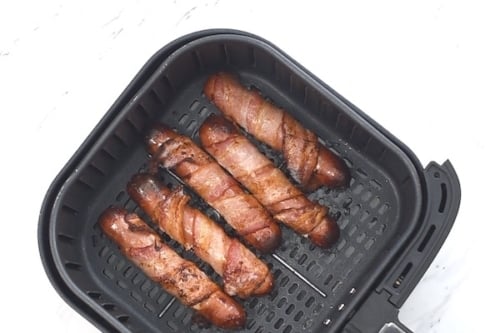 Cooked bacon wrapped hot dogs in air fryer basket