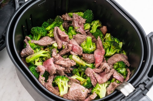 Half cooked beef and broccoli in air fryer basket