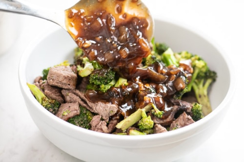 Pouring sauce over bowl of beef and broccoli