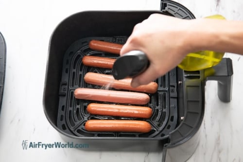 Spraying beef franks in air fryer with oil spray