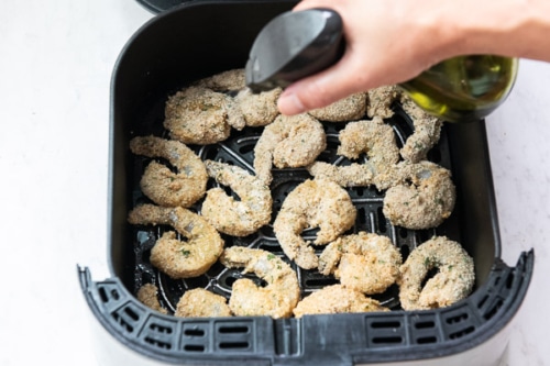 Spraying uncooked breaded shrimp in air fryer