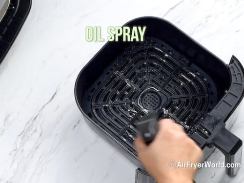 Spraying air fryer basket with oil
