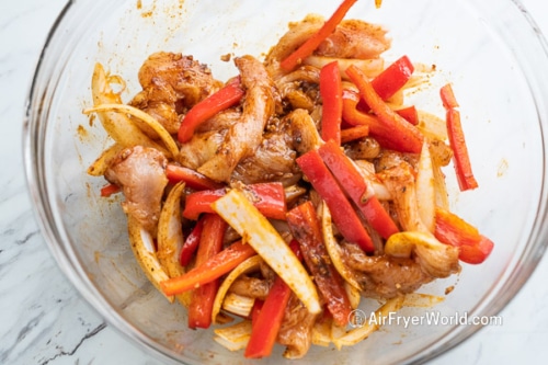 Chicken, onions, and pepper in a bowl with marinade
