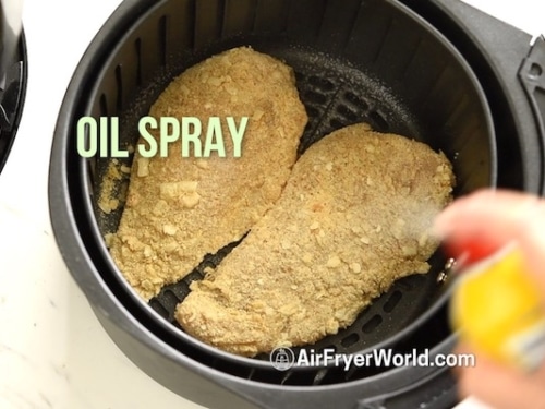 Spraying chicken breasts with oil in air fryer basket