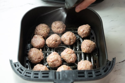 Spraying raw turkey meatballs in air fryer basket