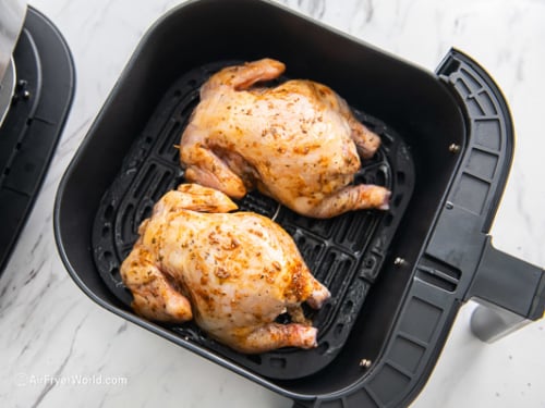 Uncooked Cornish hens in air fryer, breast side down