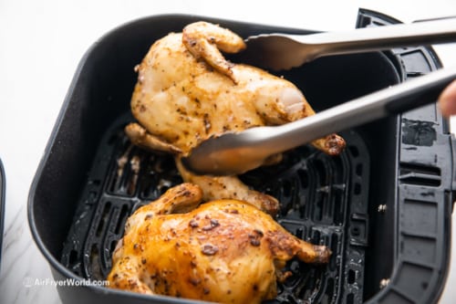 Flipping the half cooked Cornish hens over with tongs