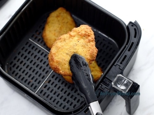 Holding with tongs an air fried breaded chicken breast