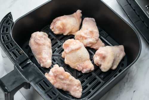 Raw frozen chicken wings in air fryer basket