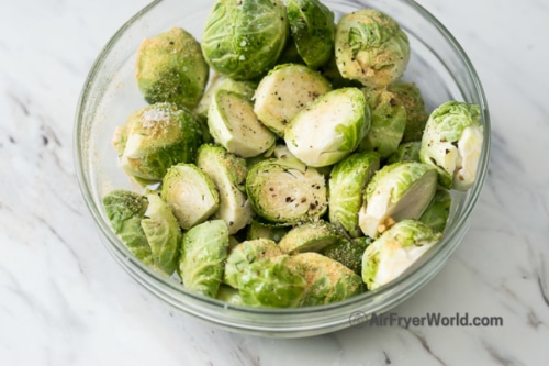Halved raw brussels sprouts in a bowl with salt and pepper