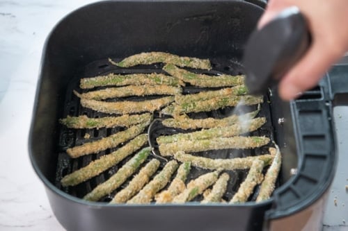 Spraying green beans with oil in air fryer basket