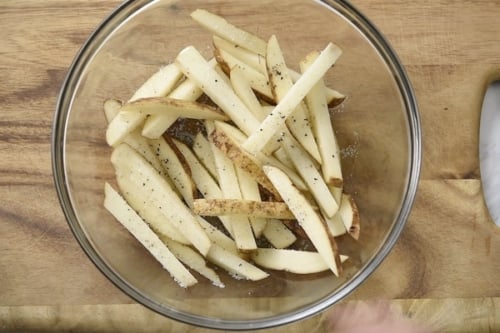 Uncooked fries in bowl with seasoning and oil drizzle
