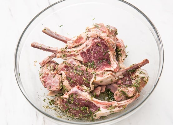 Lamb chops marinating in a bowl with rosemary