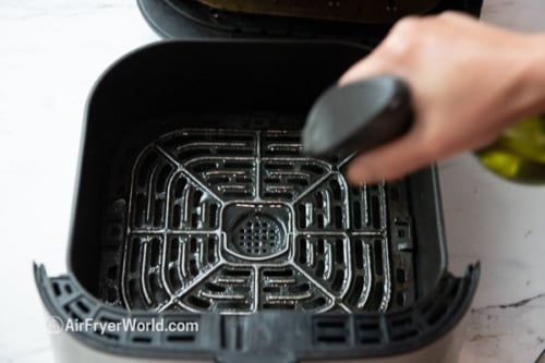 Spraying air fryer basket with oil