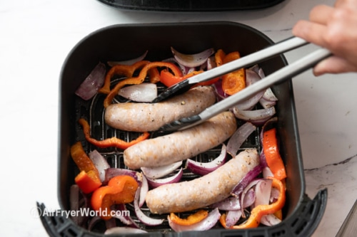 Turning half cooked sausage, peppers, and onion in air fryer basket