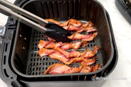 Tongs turning the bacon twists in air fryer basket