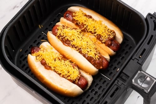 Hot dogs in buns topped with chili and cheese in air fryer basket