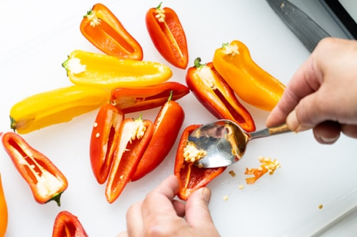 Using a spoon to remove seeds from halved mini peppers