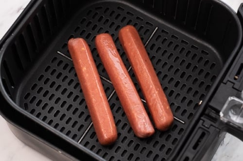 Hot dogs sprayed with oil and in air fryer basket