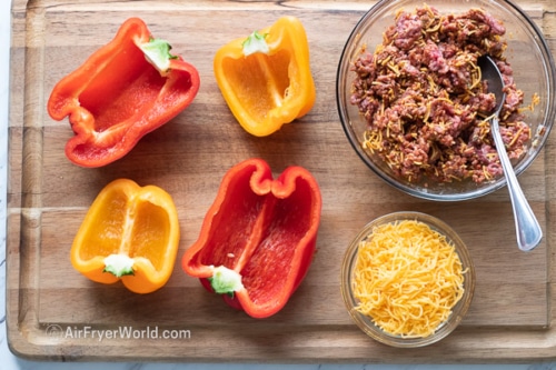 Bell peppers sliced in half on a cutting board next to taco meat filling