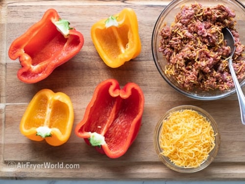 Bell peppers sliced in half on a cutting board next to taco meat filling