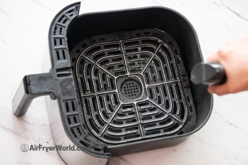 Spraying air fryer basket with oil