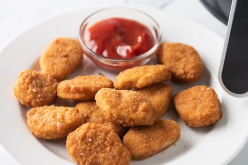 Plate of chicken nuggets with bowl of ketchup behind it