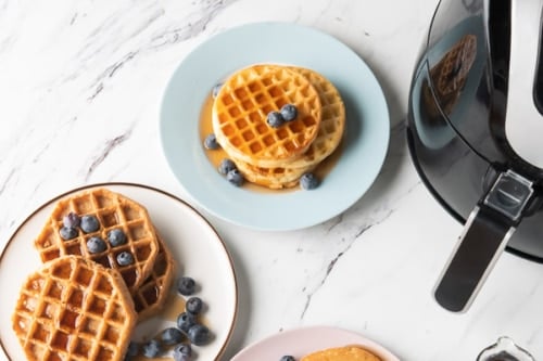 Waffles with syrup and berries on plates next to air fryer