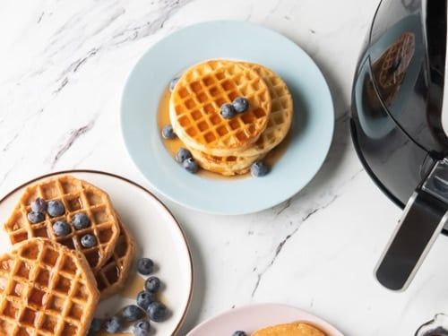 Waffles with syrup and berries on plates next to air fryer