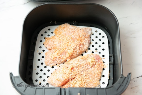 Uncooked coated fish fillets in air fryer basket