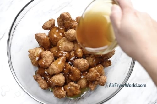 Heated orange sauce being poured over chicken in a bowl