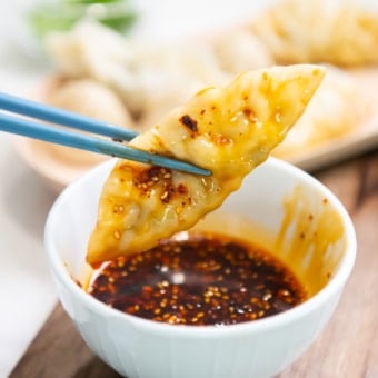 chopstick holding potsticker in dumpling sauce
