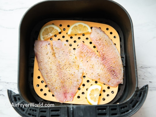 Raw tilapia filets in air fryer basket