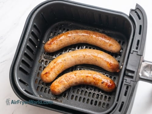 Half cooked bratwursts in air fryer basket