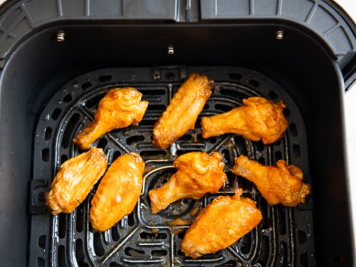 Wings tossed with buffalo sauce in air fryer basket