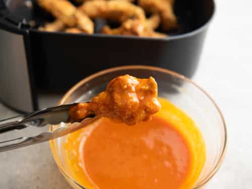 Air fried chicken wing being dipped in buffalo sauce