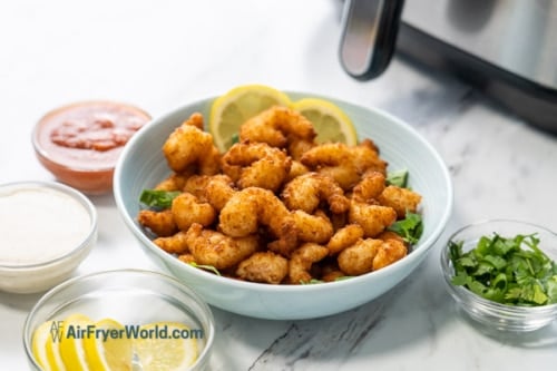 Cooked popcorn shrimp in a bowl with dips surrounding it