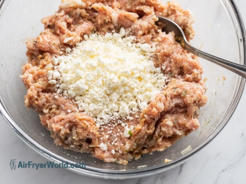 Feta being folded into meatball ingredients in a bowl