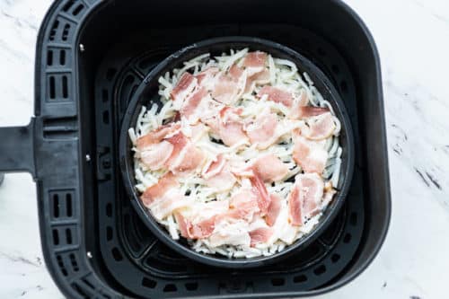 Uncooked hash browns and bacon in air fryer basket