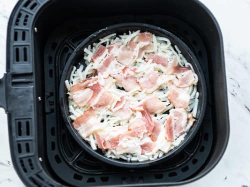 Uncooked hash browns and bacon in air fryer basket