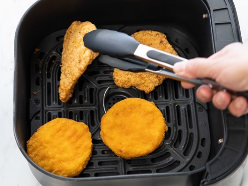 Flipping chicken breasts with tongs in air fryer basket
