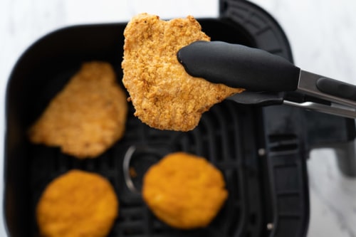 Holding cooked breaded chicken breast with tongs
