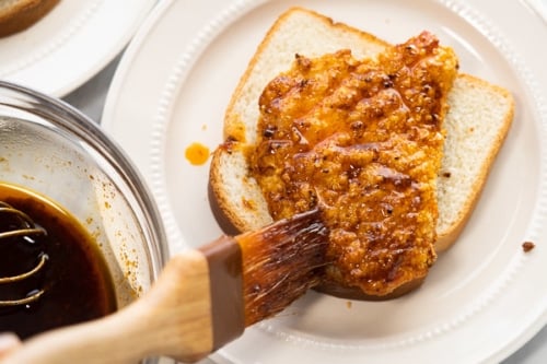 Brushing Nashville hot sauce on breaded chicken breast sitting on a piece of bread