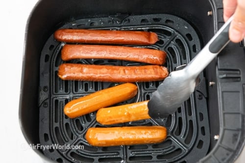 Turning plant based hot dog with tongs in air fryer basket
